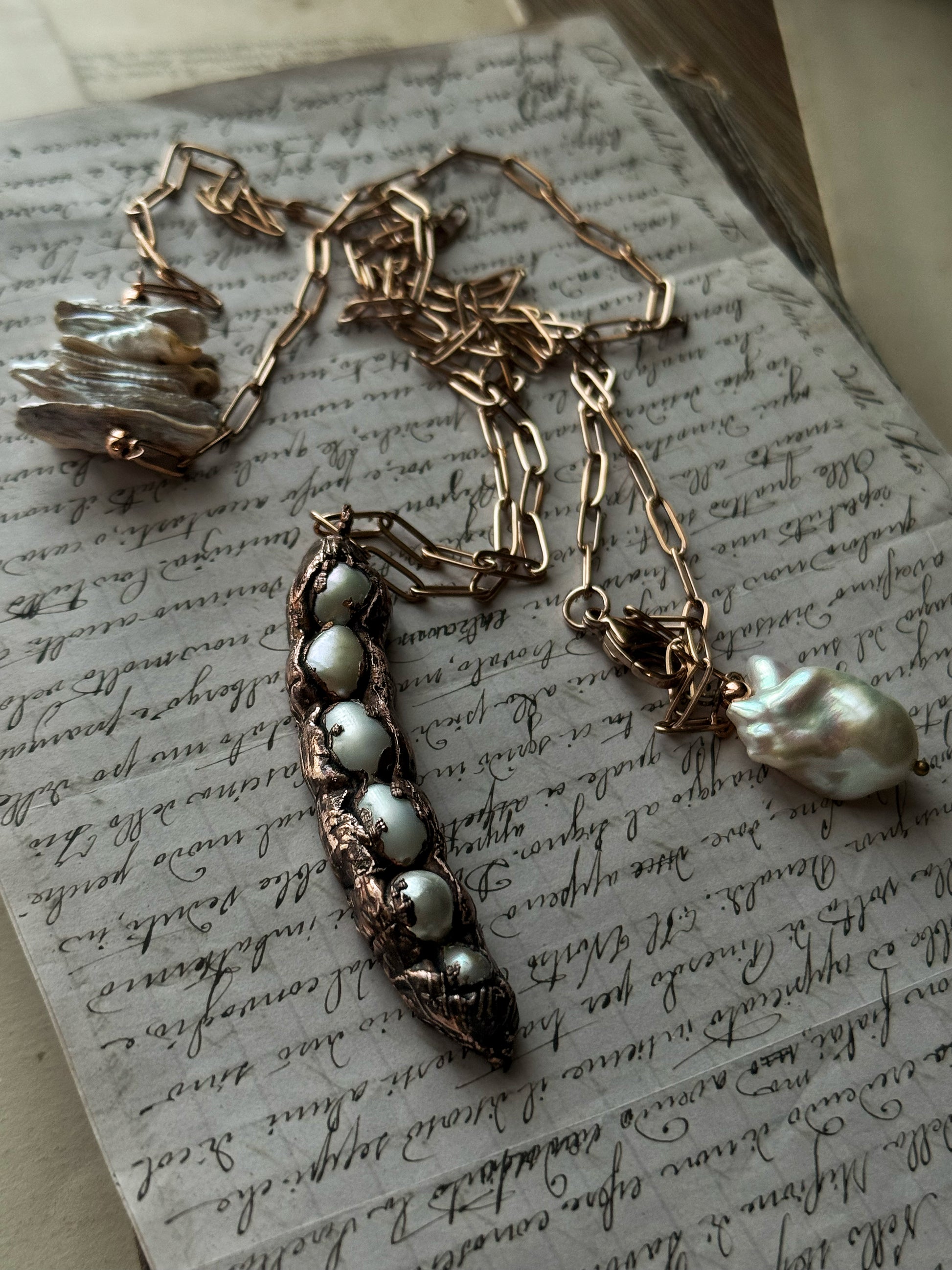 Collana lunga con ciondolo baccello in rame e sei perle d'acqua dolce, appoggiata su pagina di libro antico – Ebbijoux