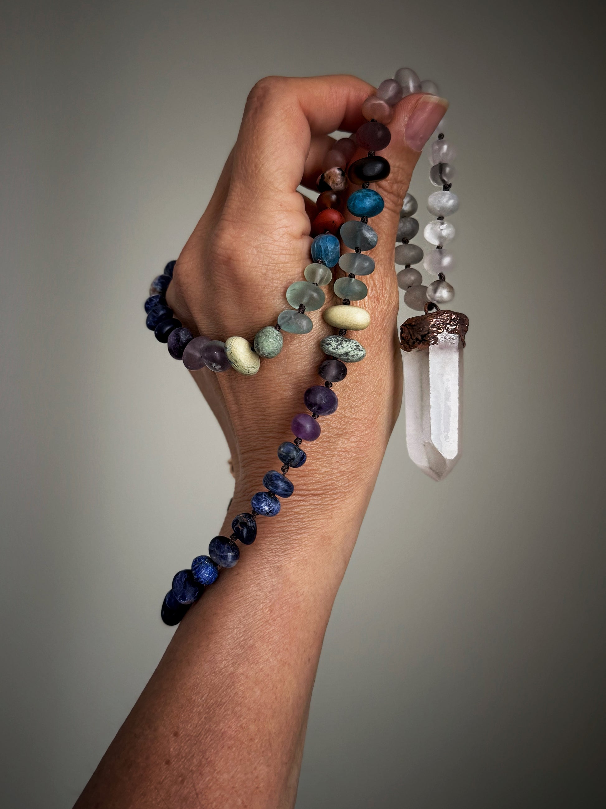Collana in pietre miste effetto matte tenuta in mano per mostrarne lunghezza e ciondolo in quarzo ialino – Ebbijoux