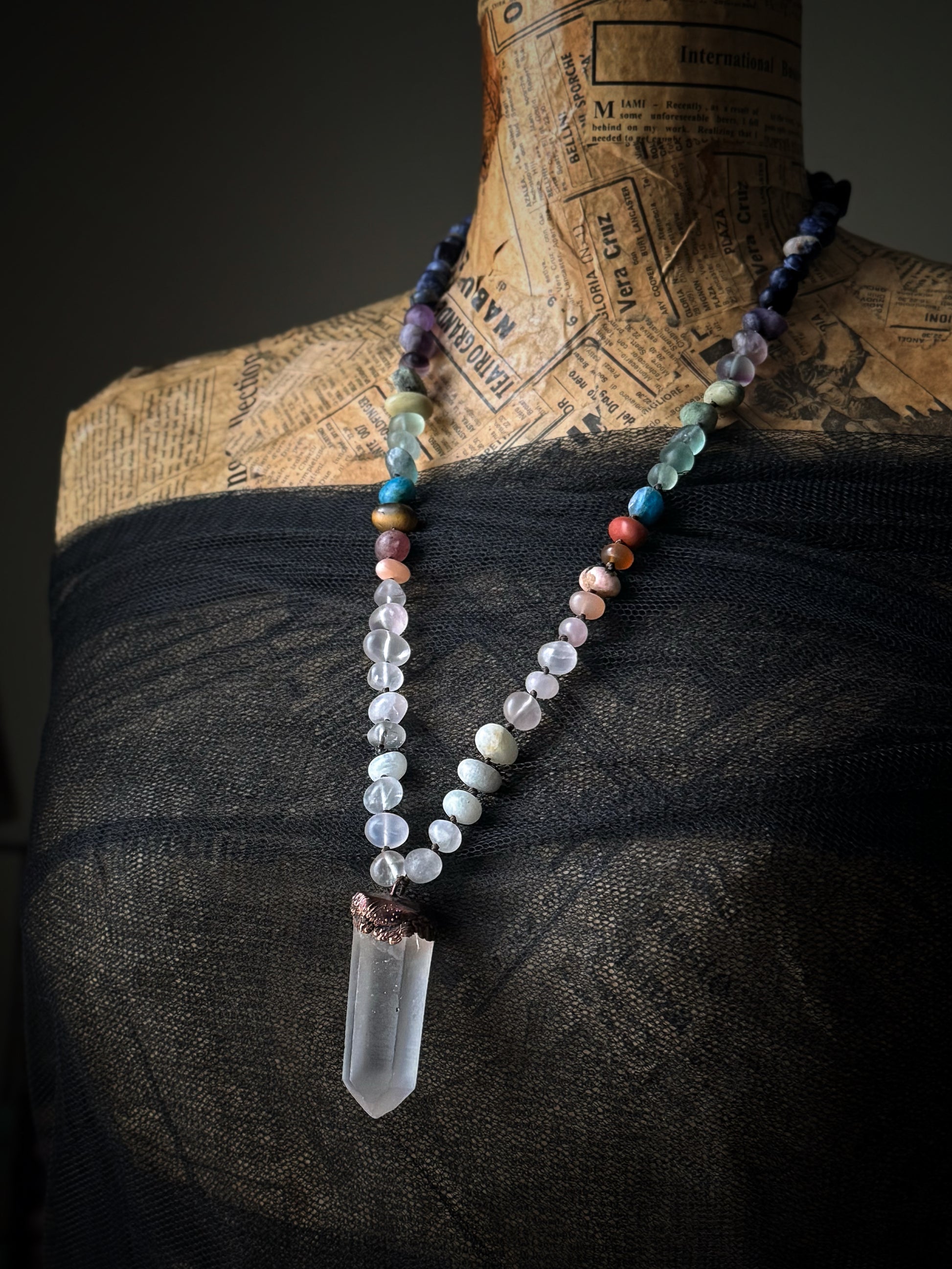 Collana lunga in pietre naturali multicolore con punta di quarzo ialino indossata su manichino vintage con pizzo nero – Ebbijoux