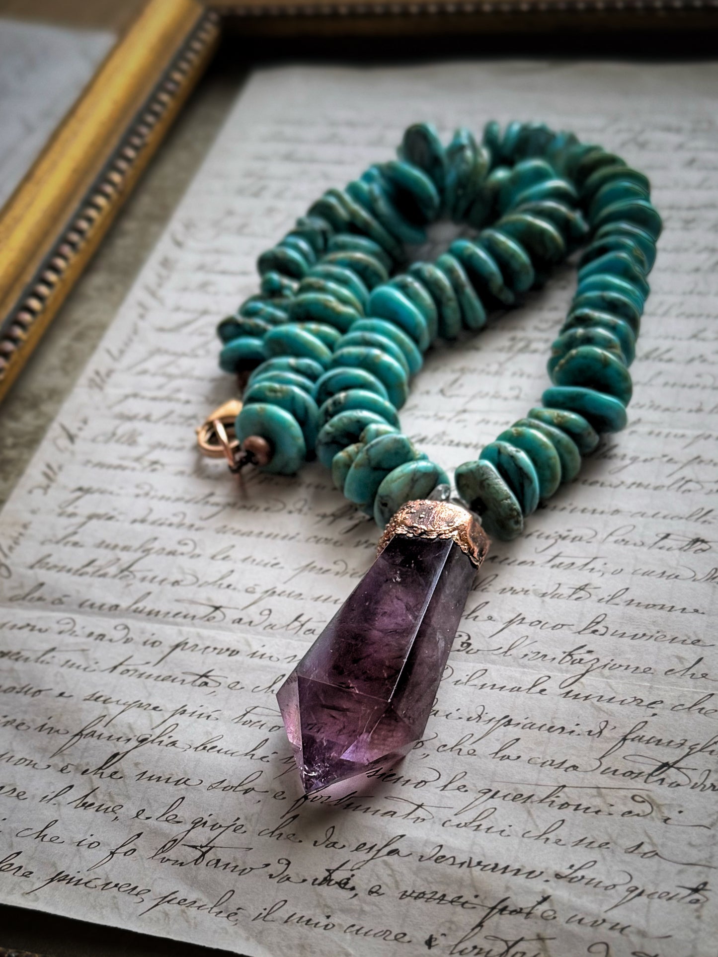 Girocollo in turchese con pendente in ametista naturale appoggiato su una lettera manoscritta accanto a una cornice dorata – Ebbijoux