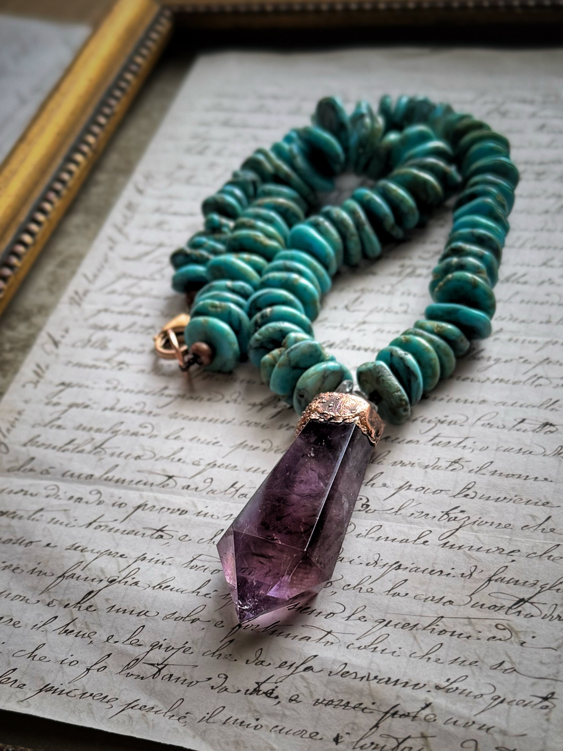 Girocollo in turchese con pendente in ametista naturale appoggiato su una lettera manoscritta accanto a una cornice dorata – Ebbijoux