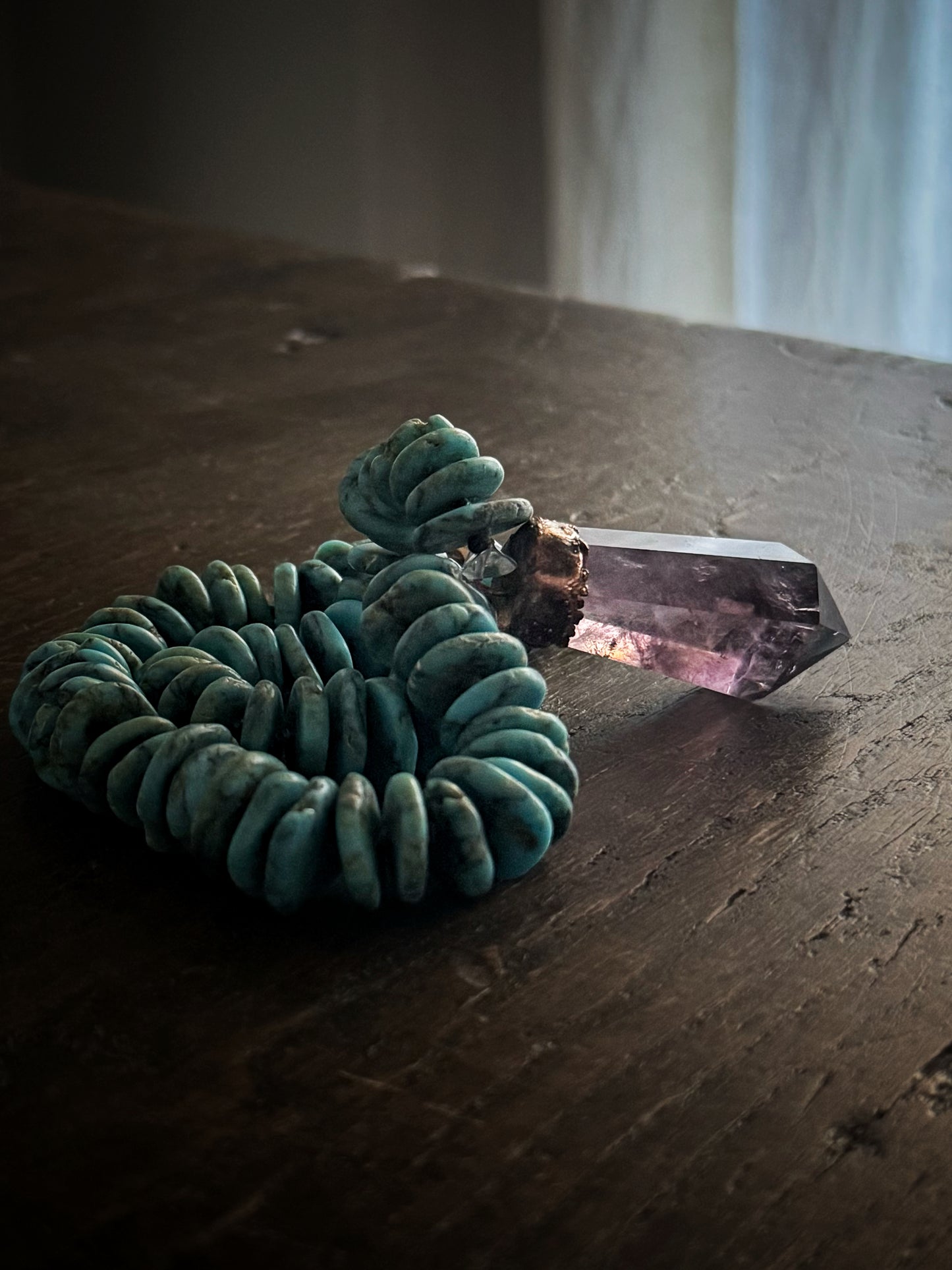 Girocollo in turchese con pendente in ametista naturale illuminato dalla luce su tavolo in legno scuro – Ebbijoux