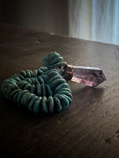 Girocollo in turchese con pendente in ametista naturale illuminato dalla luce su tavolo in legno scuro – Ebbijoux