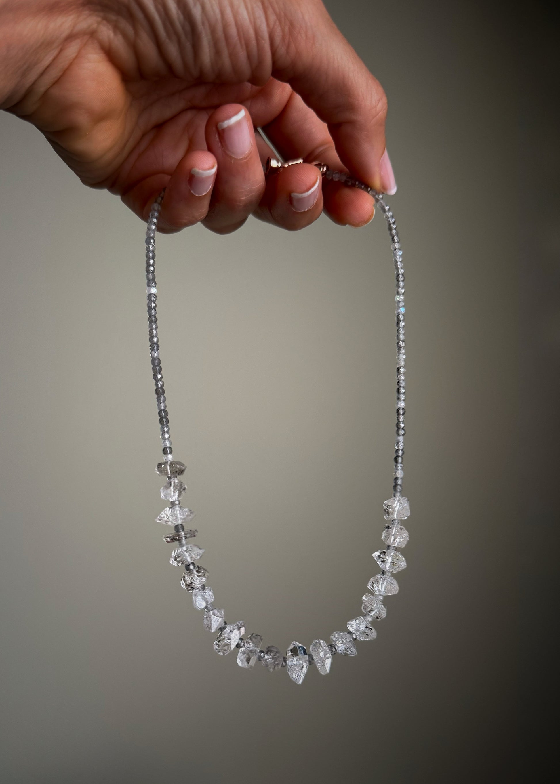 Girocollo in Labradorite e Quarzi di Herkimer tenuto in mano, pietre grigie cangianti e cristalli trasparenti al centro, chiusura oro rosa — Ebbijoux