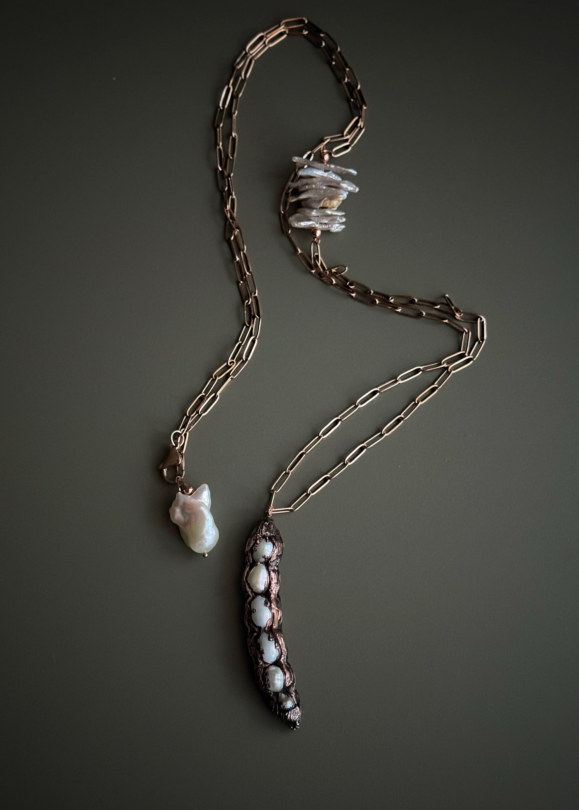 Collana lunga con baccello in rame e perle barocche chips tenuta in mano, dettaglio inserto laterale e chiusura con perla barocca – Ebbijoux