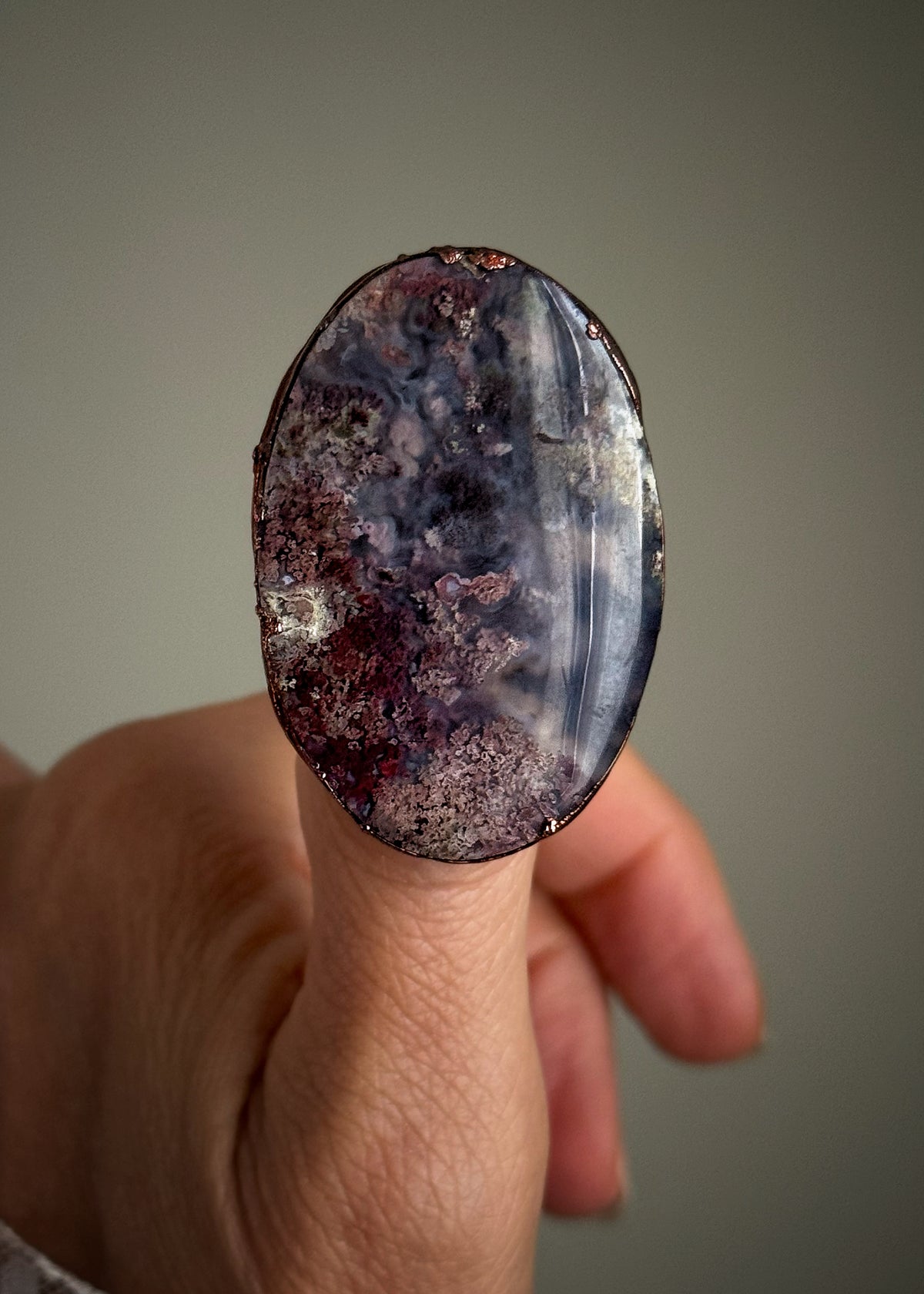 Primo piano dell’anello in rame con agata muschio ovale viola e bordeaux, indossato al dito.