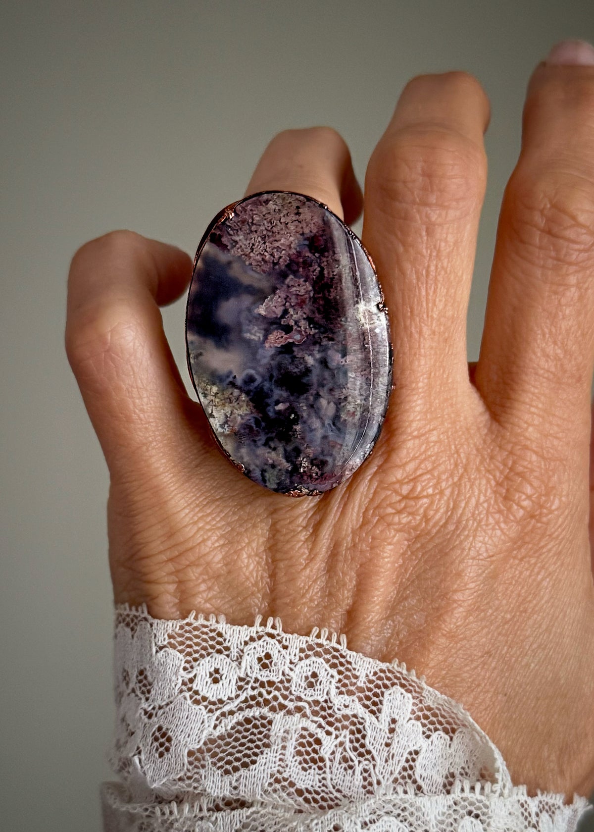 Dettaglio dell’agata muschio viola e burgundy e del bordo in rame, con l’anello indossato.⠋